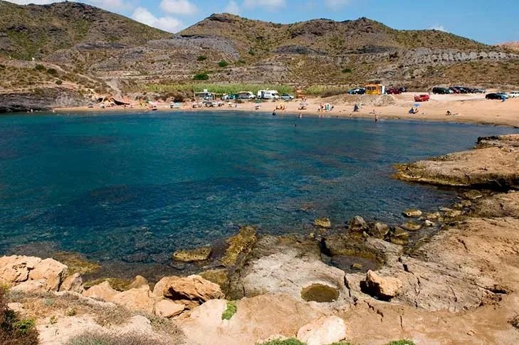 Cala Reona vista desde lo alto, con agua turquesa, rocas en primer plano y la ladera de matorral