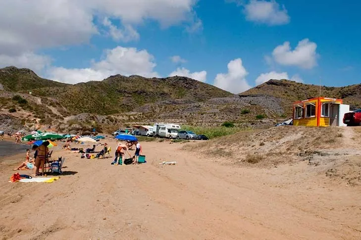 Caseta de chiringuito de temporada en la arena de Cala Reona, con las colinas áridas de Calblanque detrás