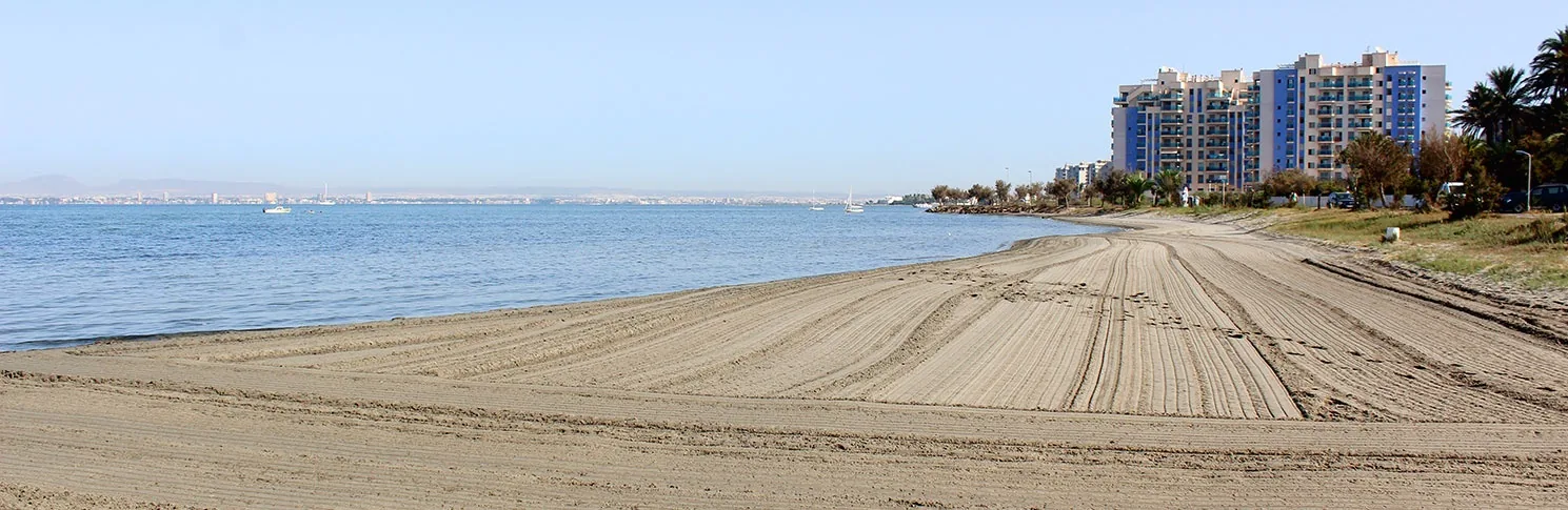 Arena rastrillada de Playa Chica con el Mar Menor sin oleaje y los edificios al fondo