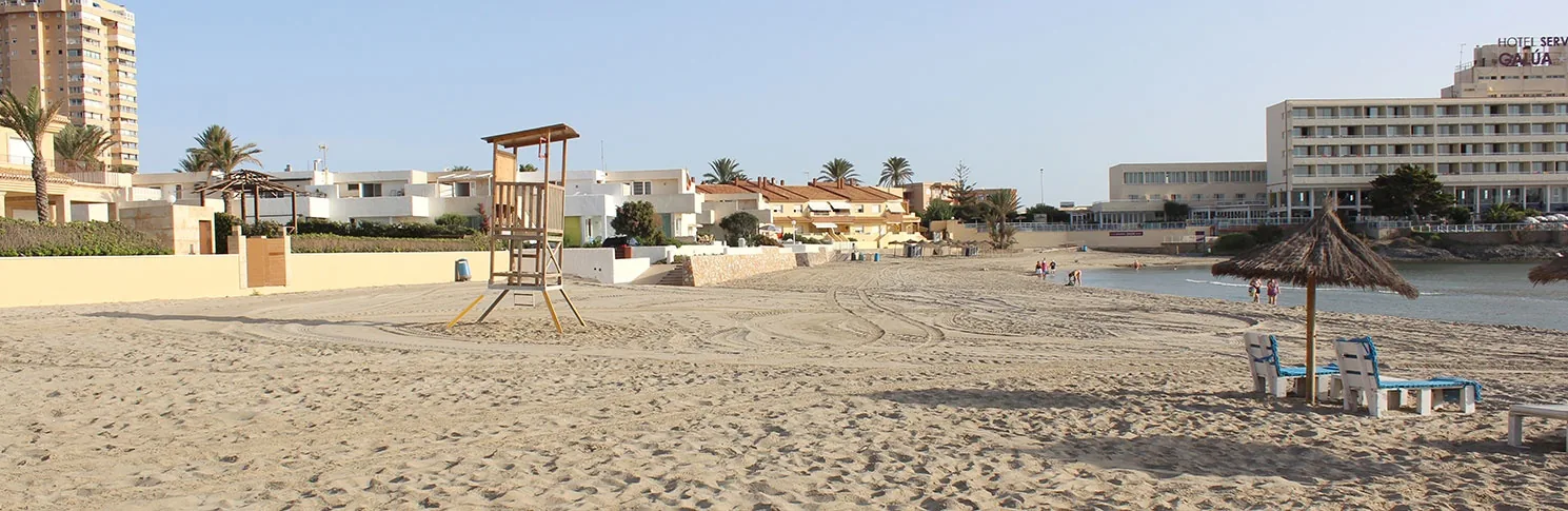 Torre de socorrista sobre la arena de Playa Galúa, con las sombrillas y los edificios detrás