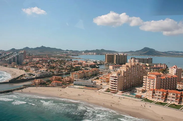 Vista aérea de La Manga a la altura de Playa Galúa, con el Mediterráneo, los edificios y la sierra al fondo