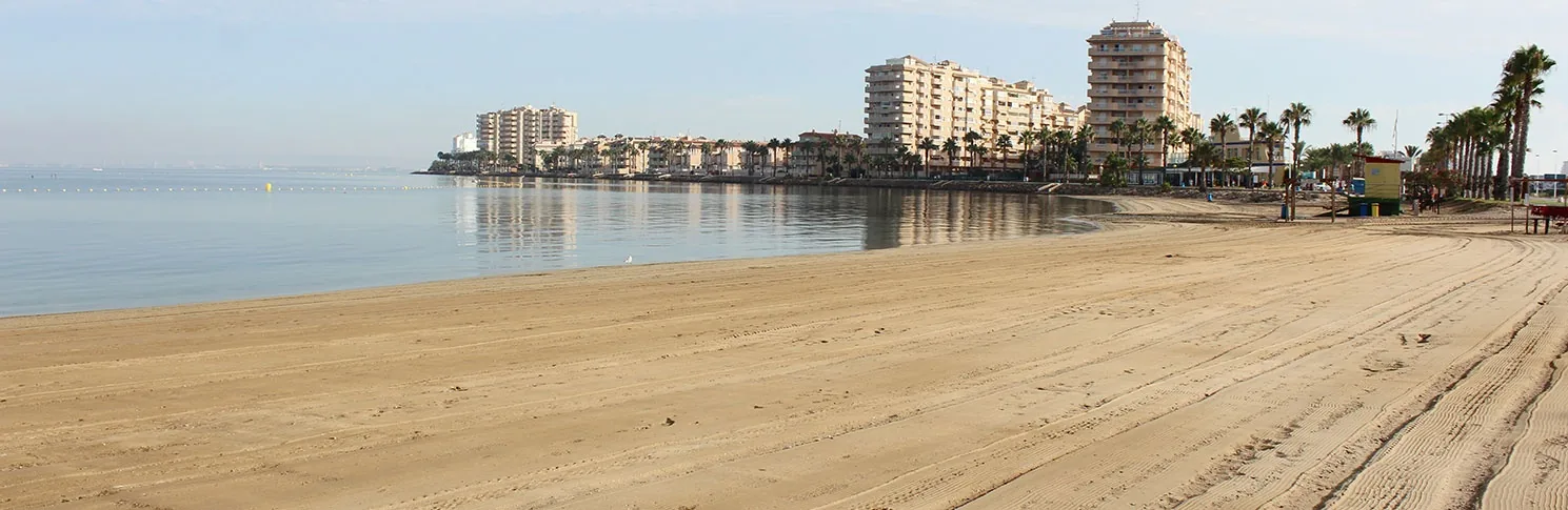 Arena rastrillada de Playa Mistral con el espigón y los edificios de La Manga al fondo