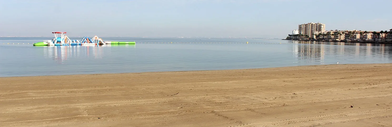 Playa Mistral con juegos hinchables sobre el agua plana del Mar Menor y los edificios de La Manga al fondo