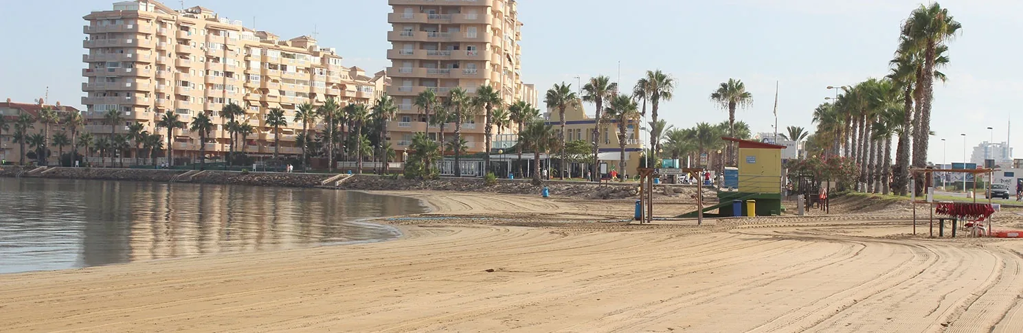 Arena de Playa Mistral con palmeras, casetas de servicio y bañistas junto al agua en calma del Mar Menor