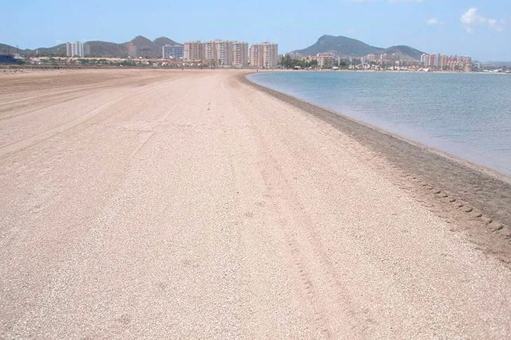 Arena clara y ancha de Playa Paraíso junto al Mar Menor, con la sierra y los edificios al fondo