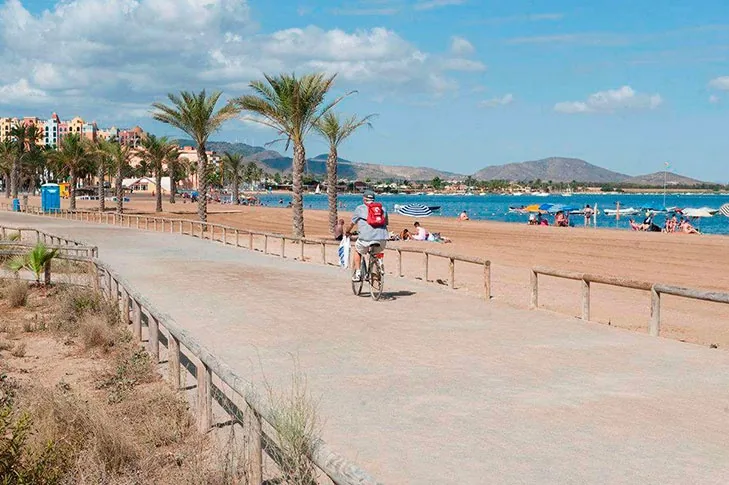Paseo de madera de Playa Paraíso con un ciclista, sombrillas y bañistas en la arena