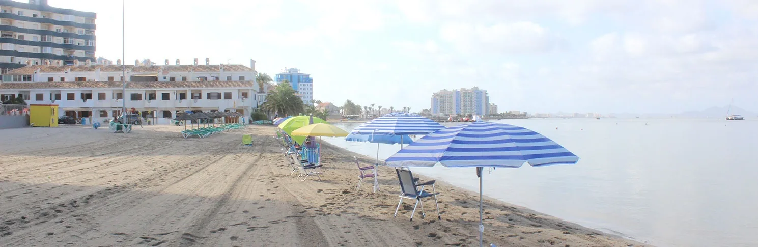 Tumbonas y una sombrilla sobre la arena de Playa La Veneziola, con un edificio blanco al fondo