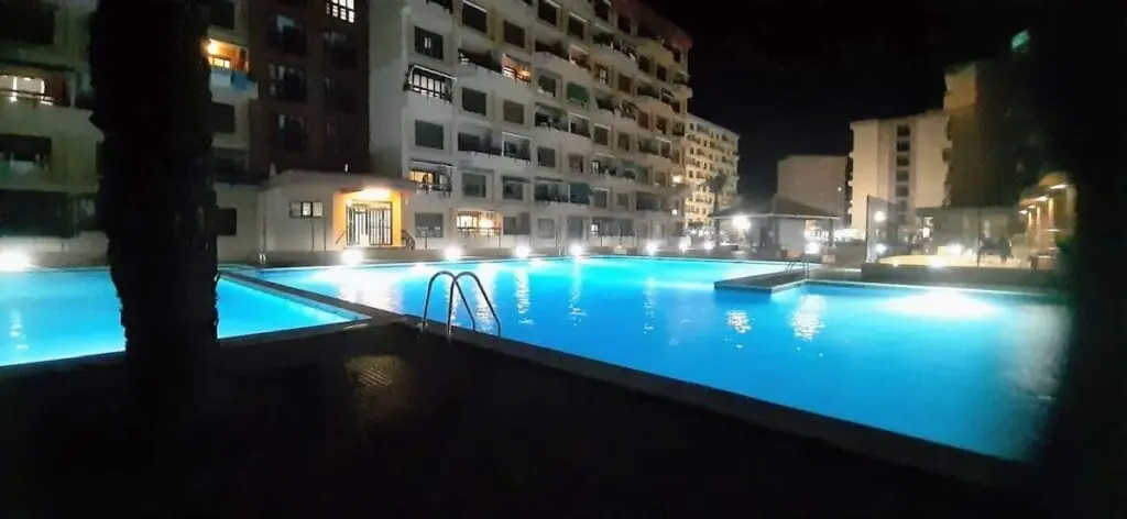 Piscina iluminada de noche en una urbanización gestionada por Arena Inn