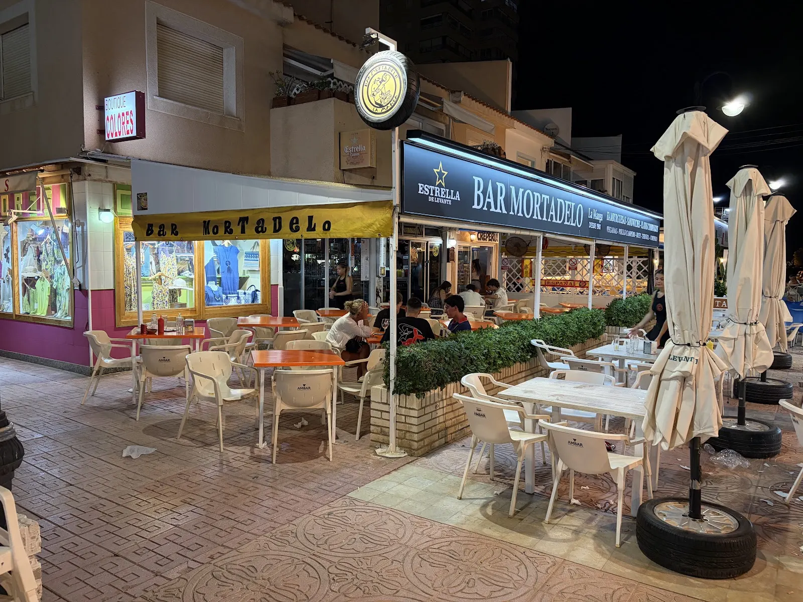 Fachada iluminada de Bar Mortadelo de noche, con clientes en la terraza