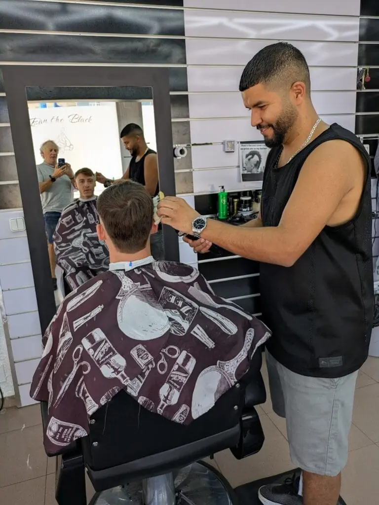 Barbero arreglando el corte de un cliente frente al espejo en Issan The Black