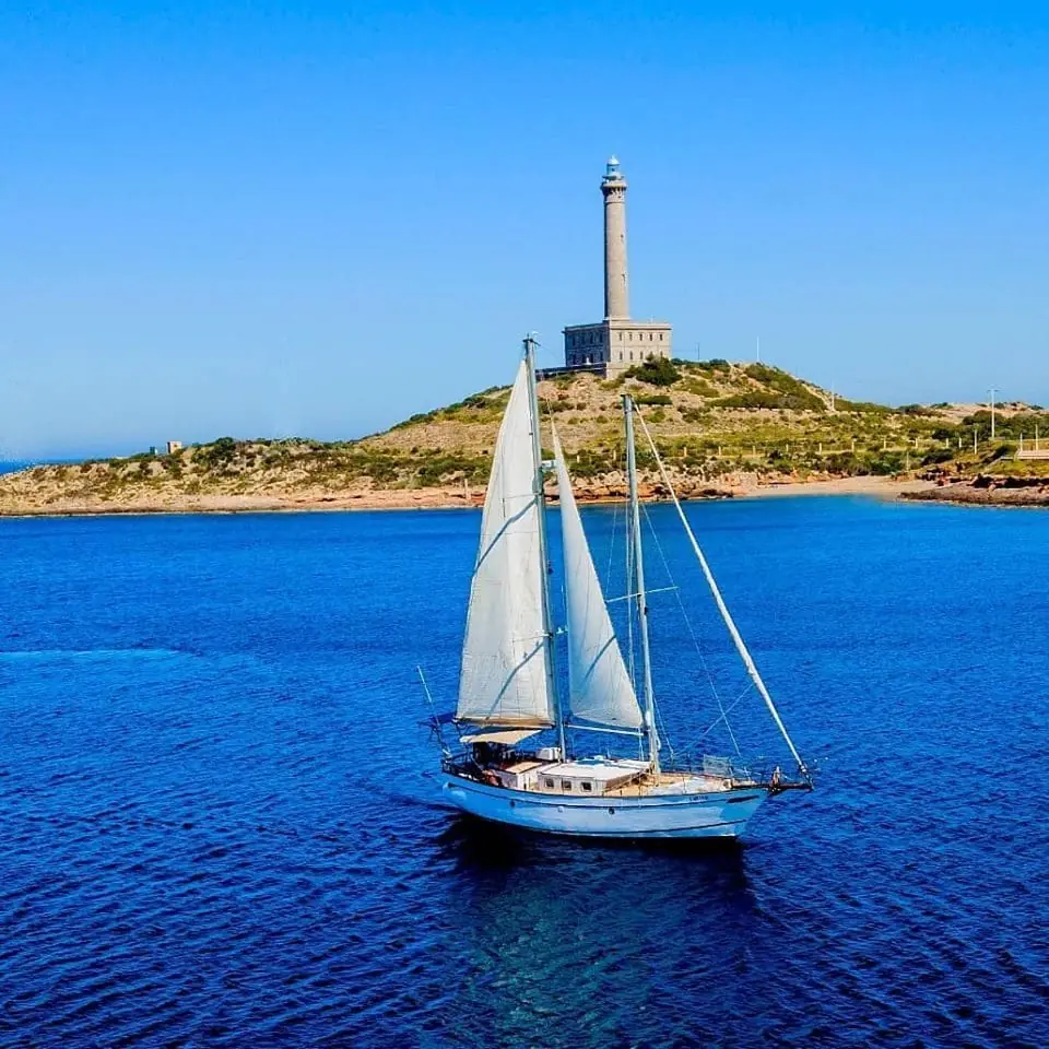 Velero de madera de Djinn Charter navegando frente al Faro de Cabo de Palos