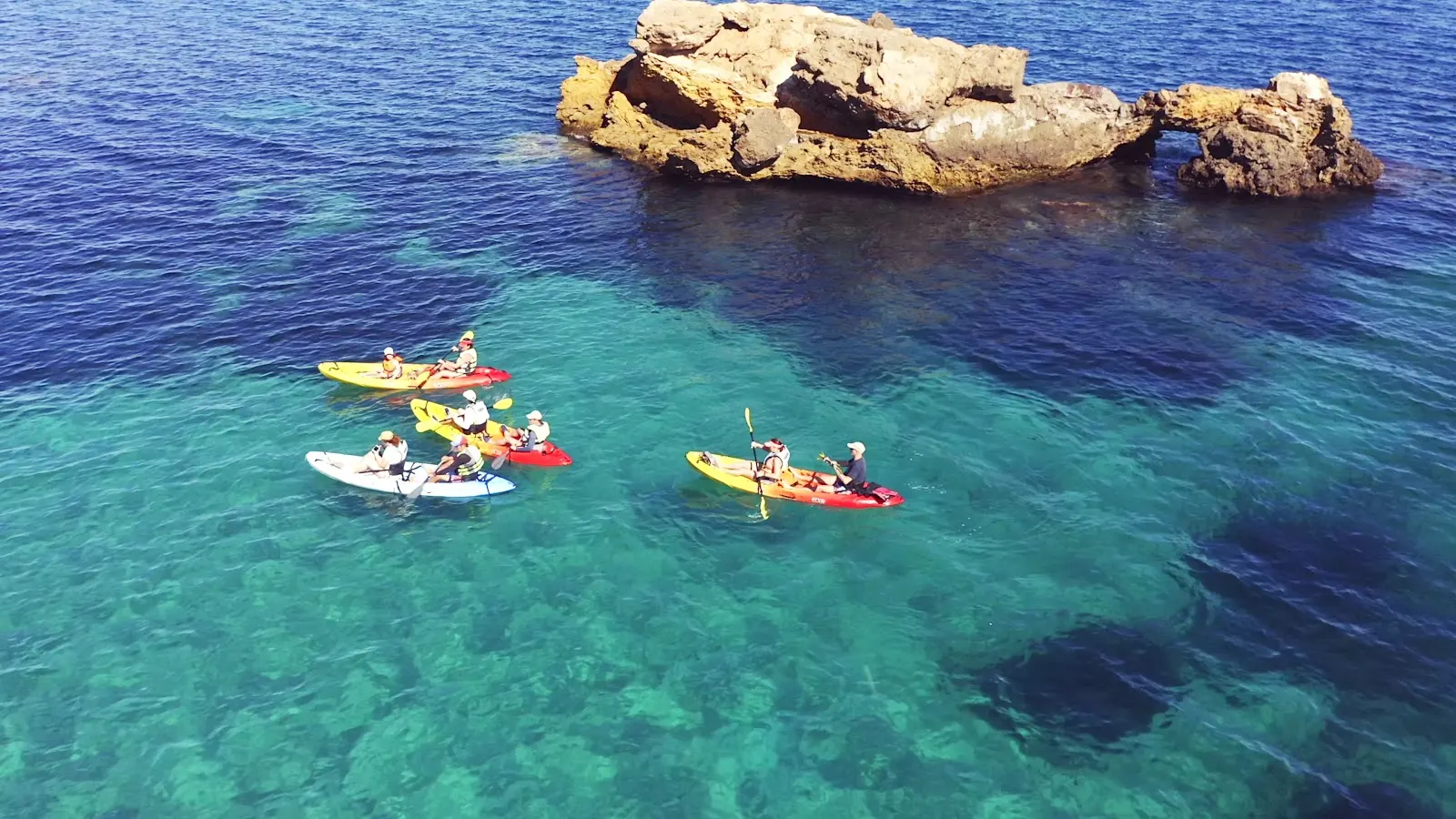 Grupo de kayaks de dKayak navegando junto a una formación rocosa en el mar