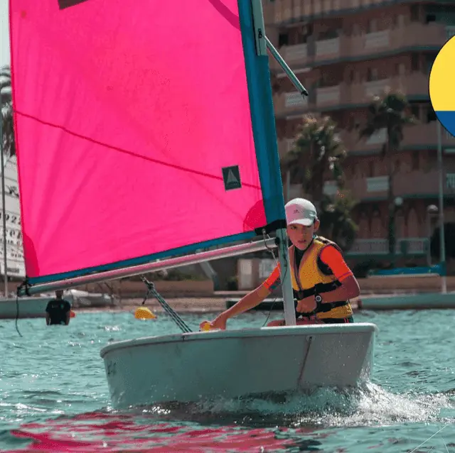 Niño navegando en un Optimist con vela rosa en Escuela de Vela Sandrina