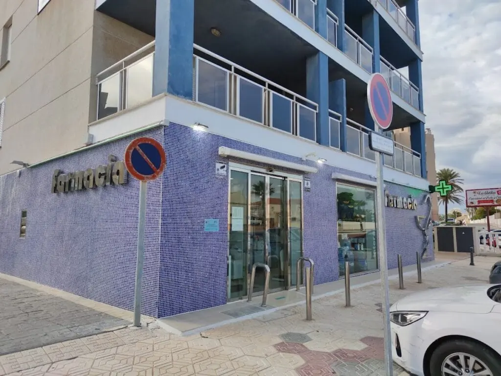 Fachada de Farmacia La Manga Centro, azulejo azul y cartel Farmacia con cruz verde, km 8 Gran Via de la Manga