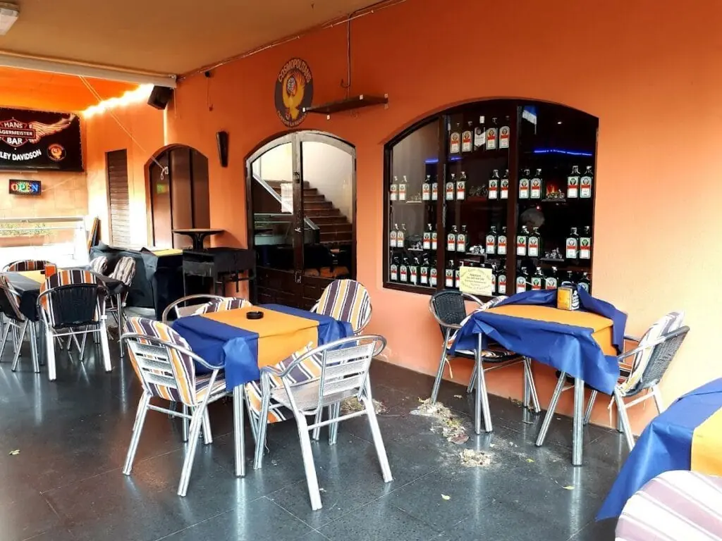 Terraza cubierta de Hans Bar con mesas y expositor de bebidas