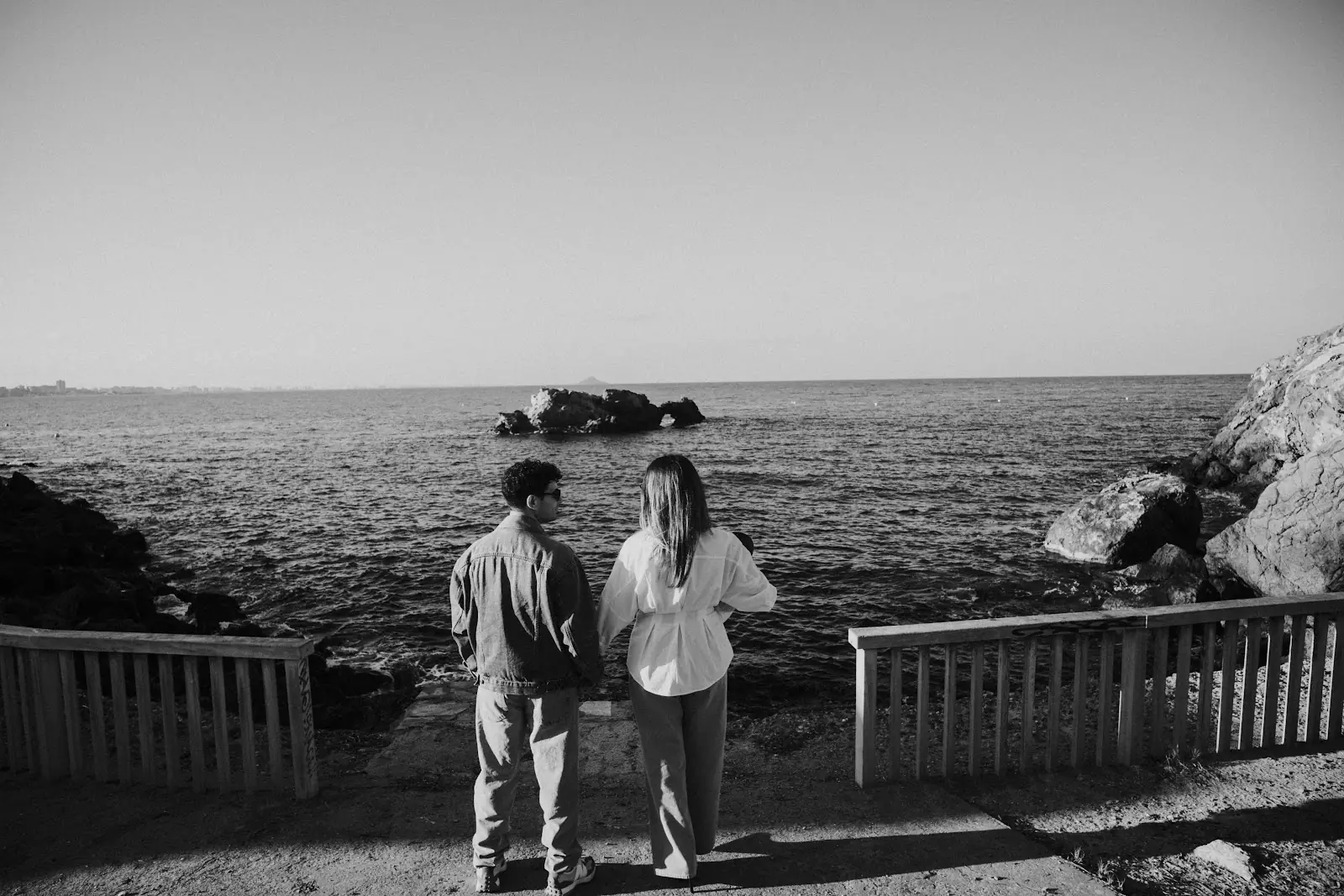 Pareja en blanco y negro contemplando el mar junto a unas rocas, fotografía de José Espinosa
