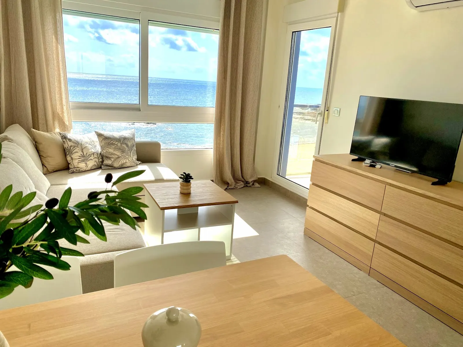 Salón del apartamento con sofá, televisor y ventanal con vistas al mar