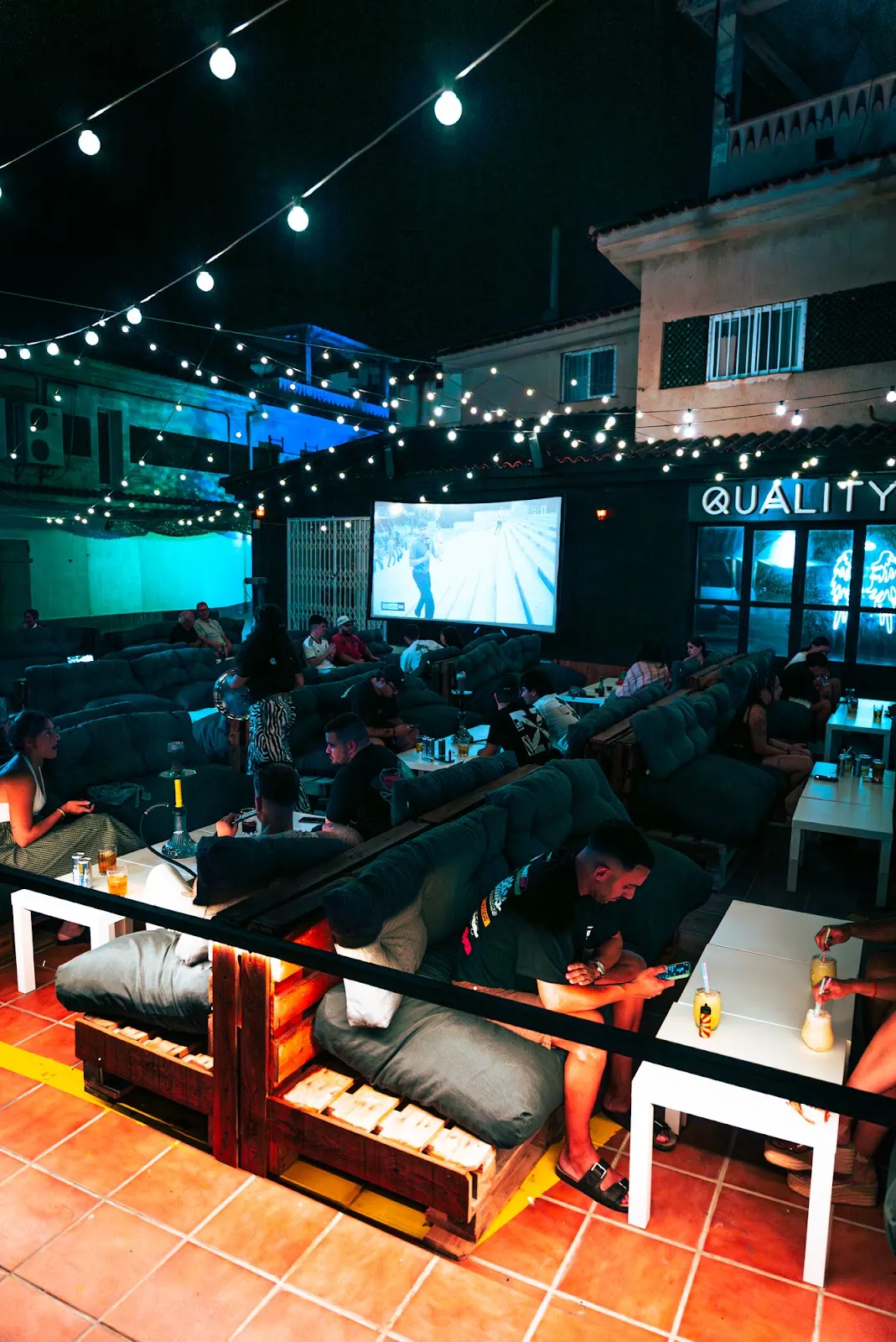 Terraza de Quality Pub con proyección en pantalla grande y ambiente nocturno