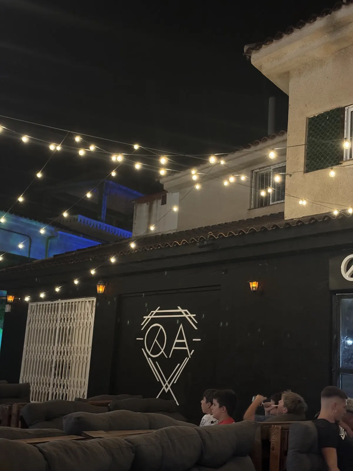 Exterior of Quality Pub at night, with strings of lights and the QA logo