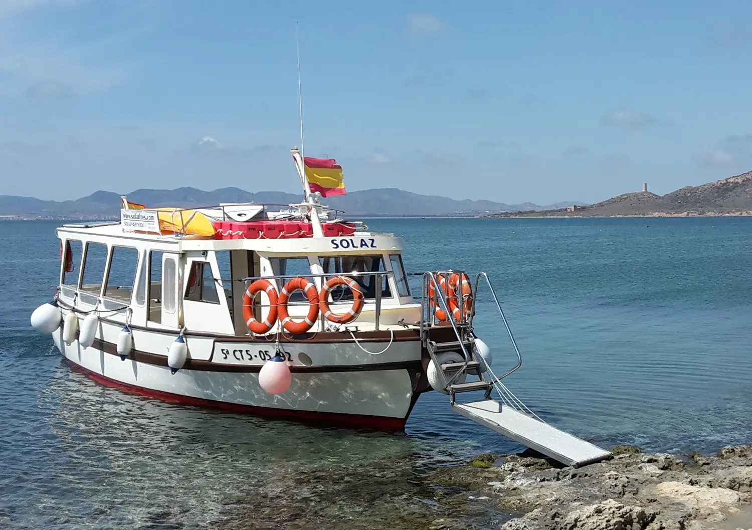 Barco Solaz atracado con pasarela desplegada junto a la costa rocosa de la Isla Grosa
