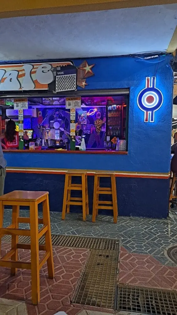 Barra y taburetes de Ya Te Vale indie bar, iluminados de noche